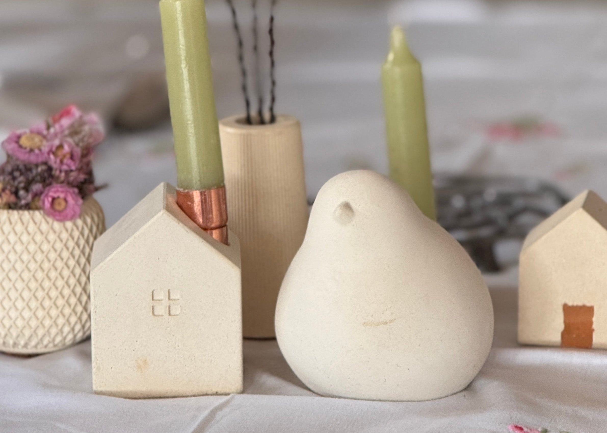 Set of decorative concrete items including a bird-shaped object, house-shaped objects, and candles on a textured surface.
